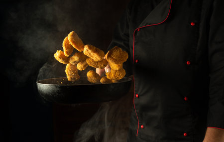 Cooking crispy nuggets. The chef tosses hot nagits into the pan. The concept of a large kitchen for a hotel with an advertising space.の写真素材