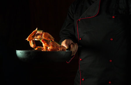 Cooking shrimp in the restaurant kitchen. Flight of prawn over a frying pan in the chef's hand. Dark space for recipe or menu.の写真素材