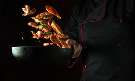 Delicious prepared shrimps in the fry pan in hand chef. Roasted shrimps with herbs. Seafood and shellfish. Shrimps Prawns grilled with spices on cast pan.の写真素材