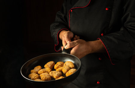 The chef is frying chicken nuggets in a frying pan. The concept of cooking nagits in the restaurant kitchen. Free space for advertising on a black background.の写真素材
