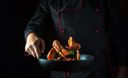 The chef cooks shrimp in a pan with herbs. The concept of cooking seafood and vegetarian healthy food on a black background with space for a recipe or menu.の写真素材