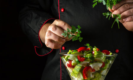 The cook adds fresh parsley to a vitamin salad for lunch. The concept of preparing a vegetarian dish with the hands of a chef.の写真素材