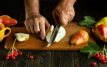 Close-up of a man's hands with a knife slicing ripe pears to serve on the table for dessertの写真素材