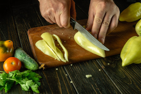 The chef cuts yellow peppers on a cutting board to prepare a vitamin salad. Delicious vegetarian food for lunch. Asian cuisine.の写真素材