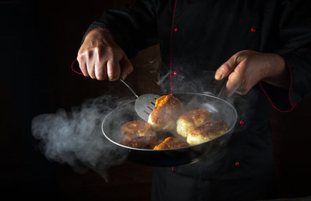The chef is preparing oladki in a frying pan. The concept of preparing Ukrainian national dish or bliny in the kitchen. Black space for recipe or menu.の写真素材
