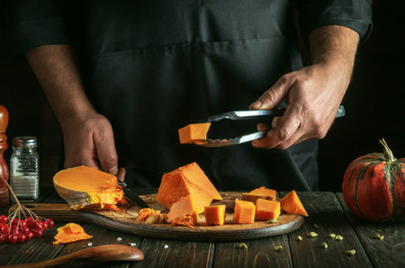 A professional chef prepares diced pumpkin filling for American pumpkin pie. Tool in the hand of a cook with a cube of raw pumpkin. A festive traditional dish popular all over the world.の写真素材