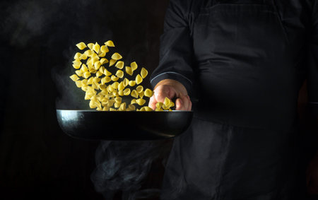 The chef is preparing a pasta dinner in a frying pan. Healthy vegetarian food and dishes recipe. Free advertising space on a dark background.の写真素材