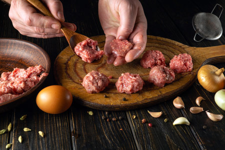 Cooking meatballs on the kitchen table from minced meat. Chef hands close-up with spoon and minced meat while making cutlets.の写真素材