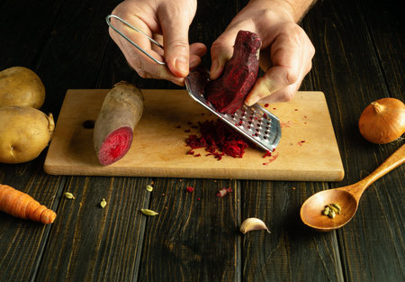 Grating red beets with a grater in the hands of a cook. Preparing vegetable dish in tavern kitchen.の写真素材