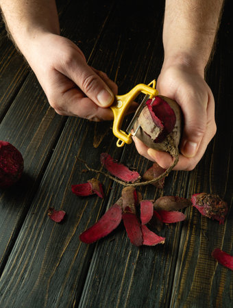A cook peels beets for grilling or for preparing vegetable dishes. On a black table, a close-up of a chef hands using a vegetable peeler.の写真素材