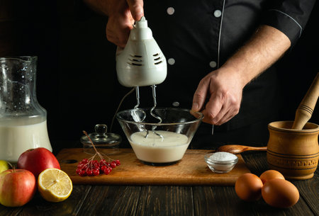 A professional chef prepares milk yogurt with fruit. Hand electric mixer in the hand of a cook. Low key concept of preparing dessert in the kitchen pub.の写真素材