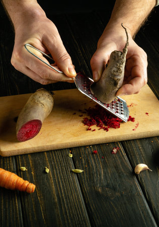 Chef hands grate beets with a grater. Low key concept of cooking vegetable salad on kitchen table.の写真素材
