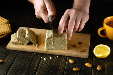 The chef uses a knife to cut sunflower halva into slices. Low key concept of serving a sweet and delicious dessert for breakfast with tea.の写真素材