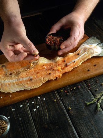 Adding spices to fish carcass before frying. The cook hands add aromatic seasoning to raw fish steak on the kitchen table.の写真素材