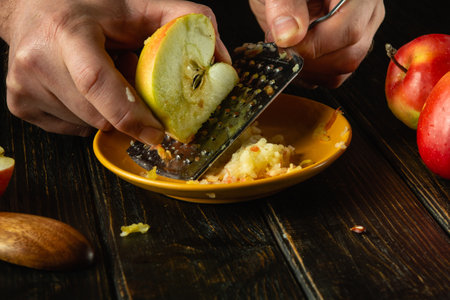Close-up of a cook hands grating apples with a grater. Preparing applesauce on the kitchen table. Space for recipe or menu.の写真素材