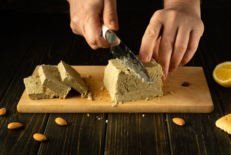 Slicing sunflower halva. A knife in the hands of a chef for cutting halva on a cutting board for dessert or breakfast. Asian cuisine.の写真素材