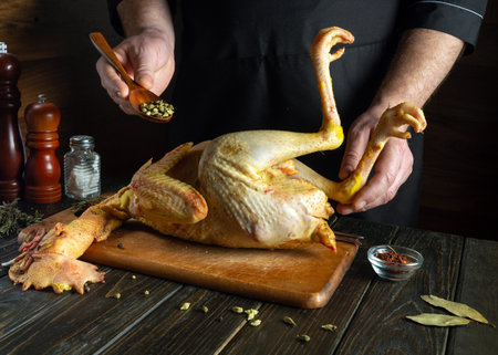 Cooking rooster on the kitchen table by the hands of the cook. The chef adds dry aromatic spices to the gray chicken on the kitchen table.の写真素材