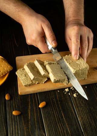 The cook uses a knife to cut sunflower halva into slices. Low key concept of serving a sweet and delicious dessert for breakfast with tea. Space for recipe or menu.の写真素材