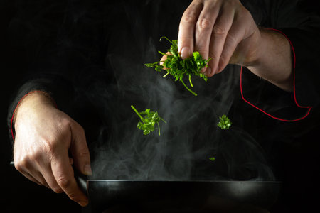 The chef adds fresh parsley to the hot frying pan by hand. Low key concept of preparing a delicious lunch in a restaurant kitchen. Grande cuisine.の写真素材