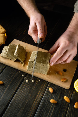 Sliced sunflower halva for dessert. A knife in the hand of a cook for cutting halva for tea with cookies and almond nuts. Advertising space.の写真素材
