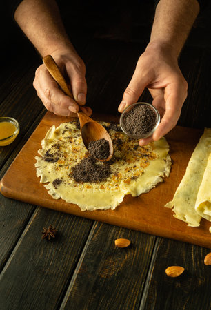 The cook adds poppy seeds to the pancakes on the kitchen table with a spoon. Low key concept for preparing the Ukrainian national dish Nalisniki.の写真素材