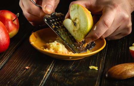 Making apple dessert. The cook grates a fresh apple with a grater in his hands on a kitchen board.の写真素材
