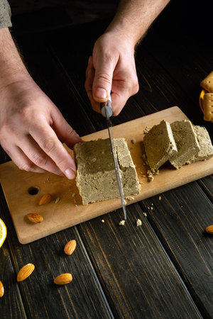 Man hands use a knife to cut fresh sunflower halva on a kitchen cutting board for dinner.の写真素材