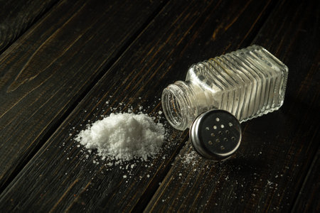 A large pile of salt is poured from a hodgepodge on a black table. The concept of excessive salt consumption, which can be the cause of various diseases.の写真素材