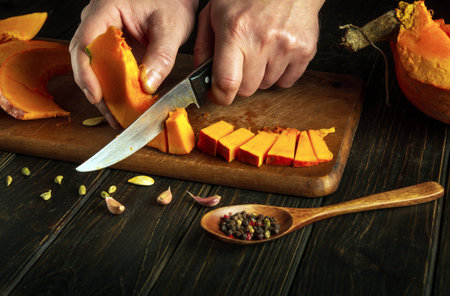 Slicing pumpkin with a knife in the hands of a man on a wooden board for preparing a vegetarian dish. Advertising space.の写真素材