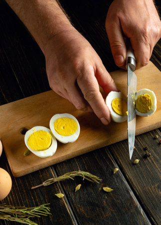 Preparing a dish of boiled eggs on the kitchen table. A knife in the hands of a cook for slicing eggs.の写真素材
