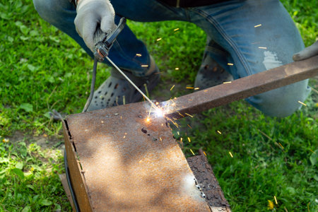 The hand of a master welder repairs metal products. Sparks from metal welding. Concept of...