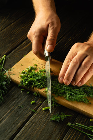 Slicing green dill on a cutting board with a knife for preparing vegetarian food by a chef's hands....