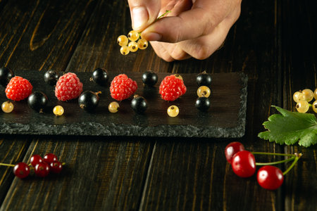 A man's hand adds ribes to a black sorting board before serving for dessert. Low-key berry diet...