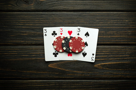 Chips and playing cards with a winning combination of three of a kind or set on a black antique...