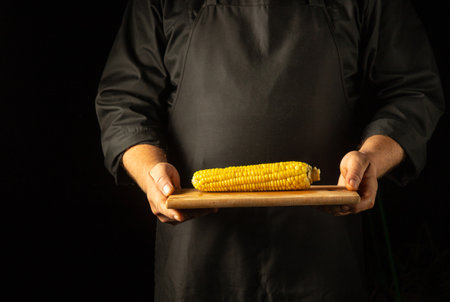 The waiter serves a head of boiled corn on a wooden cutting board in his hands. Tasty snack concept...