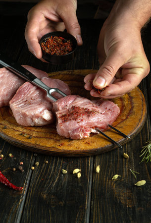 Meat steaks on a cutting board before cooking. The butcher uses his hand to add dry aromatic spices to the meat for flavor.の写真素材