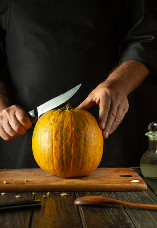 Chef tries to cut ripe pumpkin on cutting board with knife. Fruit diet concept in restaurant kitchen. American national cuisine or making pie.の写真素材