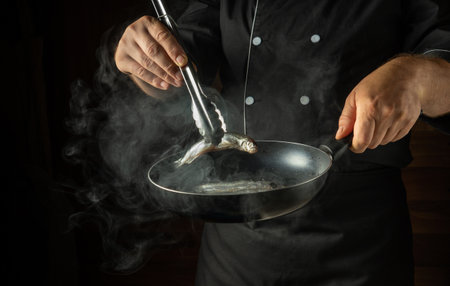 Frying capelin in a frying pan. The chef puts the small fish into the frying pan with kitchen tongs. Menu concept for a restaurant or hotel.の写真素材