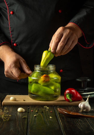 A cook manually fills a jar with bell pepper before preserving them with spices in a jar. The...