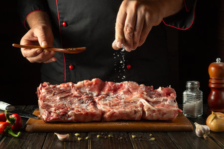 Chef sprinkles raw lamb meat with salt. Preparing a large steak of raw meat before roasting. Working environment in a hotel kitchen.の写真素材