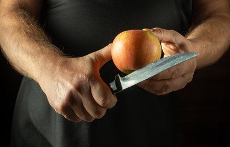 Chef trying to cut pink apple with knife. Low key concept of cooking apple dessert in kitchen.の写真素材