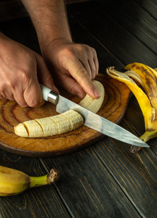 Male hands cutting ripe banana with knife on kitchen board. Concept of healthy breakfast with fruits. Advertising space.の写真素材