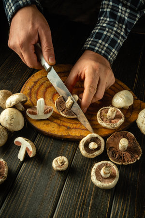 Chef hands cut mushrooms champignon with a knife on a wooden cutting board. The concept of the process of preparing a healthy mushroom diet.の写真素材