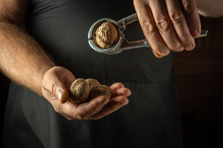 Chef peeling walnuts with his hands and a nutcracker. Close-up of cook hands with a nutcracker while...