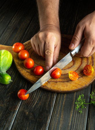 Men hands using a knife to cut cherry tomatoes to prepare a salad for breakfast at home.の写真素材