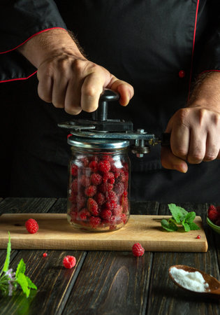 With careful hands, a chef compresses fresh raspberries into a glass jar, embracing the art of preservation. The rustic setting enhances the vibrant colors of the fruits and herbs.の写真素材