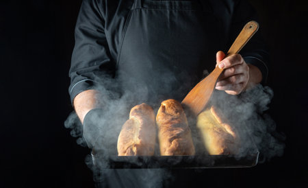 Warm pastries rest on a tray, enveloped in soft steam. A chef gently holds a wooden spoon, ready to serve these delightful treats in a rustic kitchen setting.の写真素材