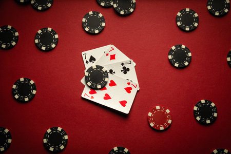 Four playing cards with a winning combination of four of a kind or quads are on a red table in a...