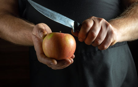A pair of hands hold a vibrant apple while a knife hovers above it, poised for cutting. Soft light...