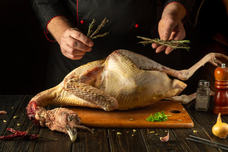 The hands of a chef prepare a large turkey, adding aromatic herbs and rosemary to create a savory dish for a fine dining experience.の写真素材